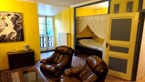 A room with a brown leather armchair, a small wooden table, a bed with a canopy, and a large painting on the wall. - Château Montegut - Private apartment in a medieval tower with Pyrenees view (Montégut)