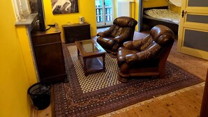 A living room with a leather armchair, a small table, a radiator, a bed with a canopy, a painting on the wall, and a window with a view. - Château Montegut - Private apartment in a medieval tower with Pyrenees view (Montégut)