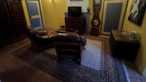 A living room with a leather sofa, a coffee table, a television, a clock, and a rug. - Château Montegut - Private apartment in a medieval tower with Pyrenees view (Montégut)