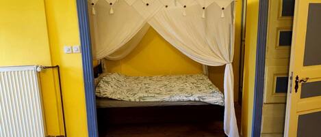 Una habitación con una cama bajo un dosel, paredes amarillas, un radiador y un sillón de cuero marrón.
