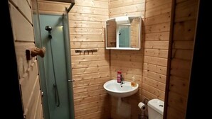 A small wooden cabin bathroom with a glass shower, a sink, and a toilet. - Château Montegut - Private apartment in a medieval tower with Pyrenees view (Montégut)