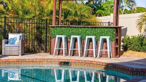 Un espace piscine agrémenté d’une pergola, de chaises longues et d’une petite terrasse avec des tabourets.