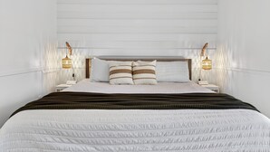 Un lit bien fait, avec un oreiller à rayures blanches et brunes, une couverture marron foncé et deux lampes de chevet au motif tissé.