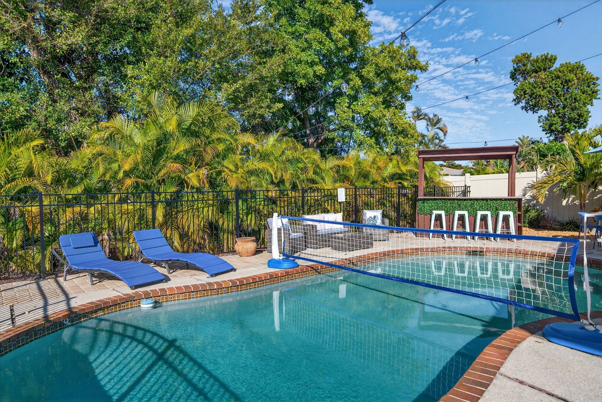A swimming pool with blue lounge chairs and a netted area, surrounded by lush greenery.