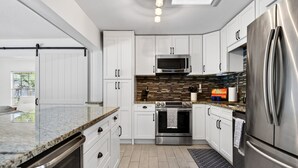 Une cuisine moderne avec des meubles blancs, un réfrigérateur en acier inoxydable, un four à micro-ondes et un pare-feu en carreaux.