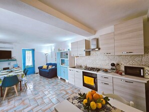 Een moderne keuken met witte kastjes, een magnetron en een fornuis. Er is een eethoek met een tafel en stoelen, en een blauwe bank op de achtergrond.