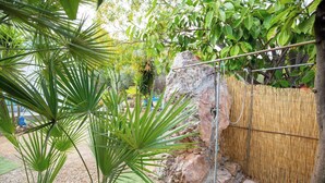 Un jardín con una formación rocosa, una cerca de bambú y plantas verdes.