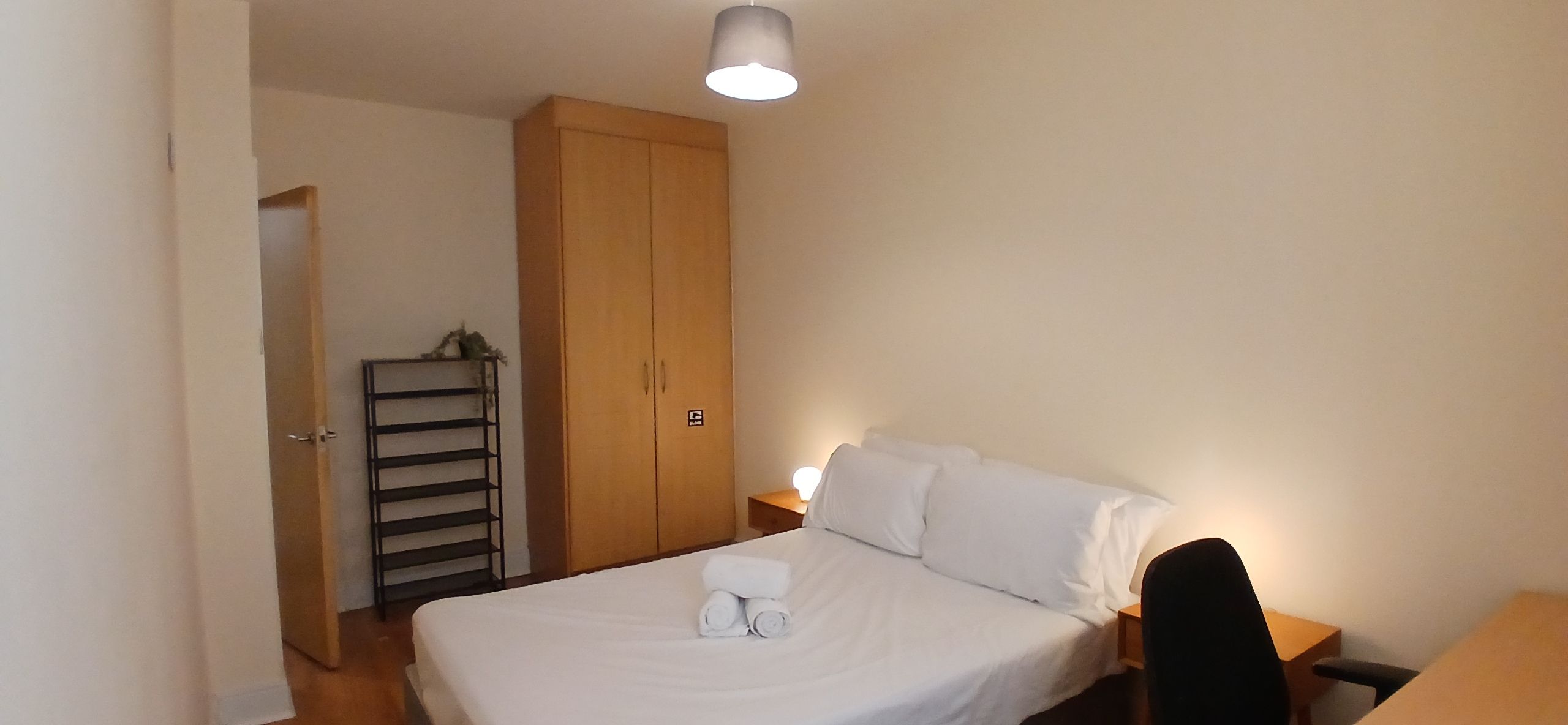 A bedroom with a bed, a wardrobe, a nightstand, and a desk.