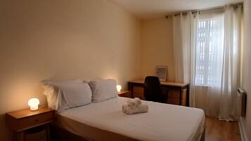 A bedroom with a bed, bedside tables, a desk, and a window with curtains.
