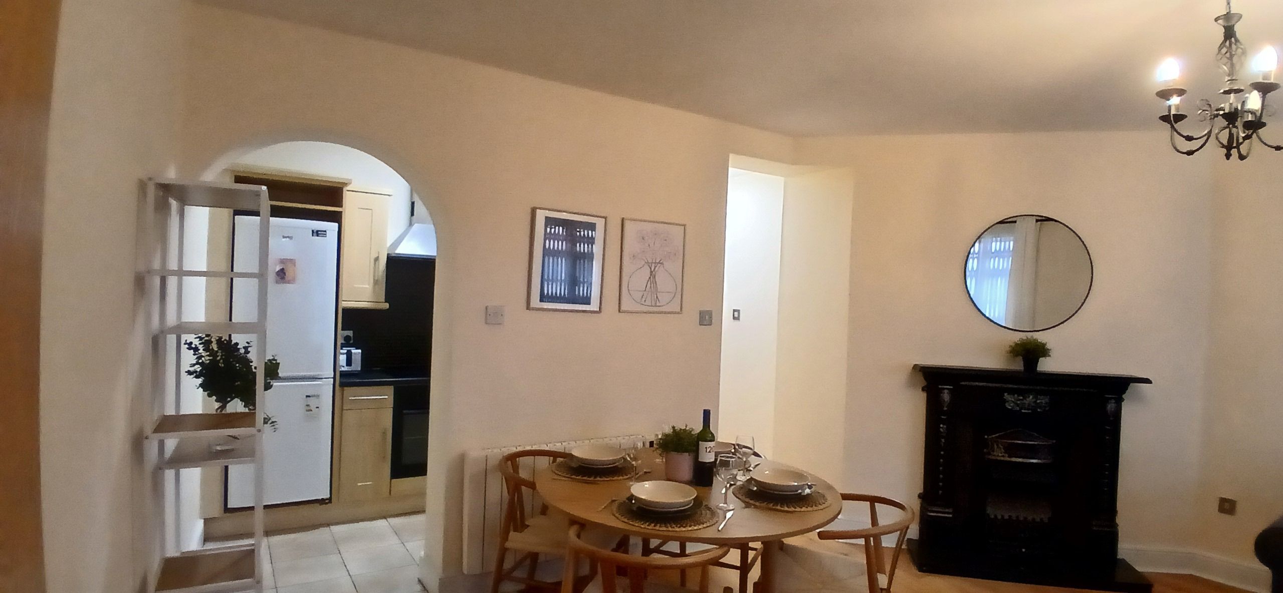 A dining area with a round table, chairs, a chandelier, and a fireplace.