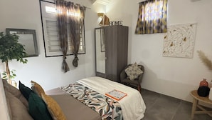 Une chambre à coucher avec un lit, une armoire, un miroir, une plante et une petite table.