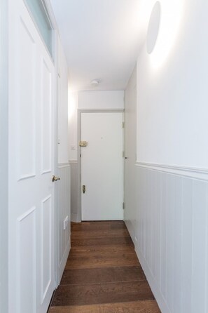 A hallway with white walls, a wooden floor, and a closed door at the end. - Modern Scandi-style 2bed Facing Vauxhall Park (London)