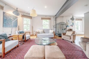 A spacious living room with a glass coffee table, multiple seating options, and large windows. - Experience London in Amazing Reconverted Gin House (London)