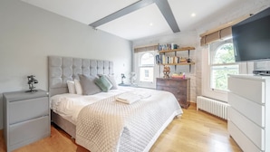 A bedroom with a bed, bedside tables, a wardrobe, a shelf with books, a window, and a TV. - Experience London in Amazing Reconverted Gin House (London)