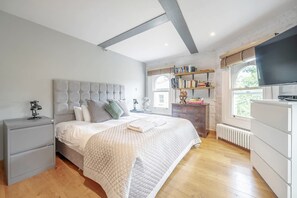 A bedroom with a bed, bedside tables, a wardrobe, a shelf with books, a window, and a TV. - Experience London in Amazing Reconverted Gin House (London)
