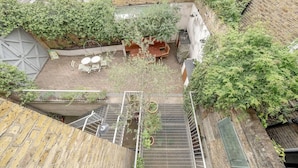 An outdoor courtyard with a wooden table and chairs, surrounded by brick walls and greenery. - Experience London in Amazing Reconverted Gin House (London)