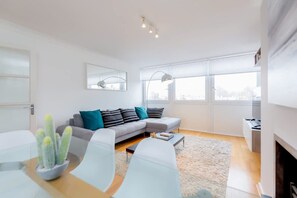 Un salon moderne avec un canapé gris, des fauteuils blancs, une table basse et un cactus.