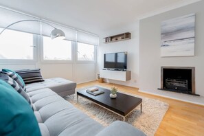 Un salon moderne avec un canapé, une table basse, un téléviseur et une cheminée.