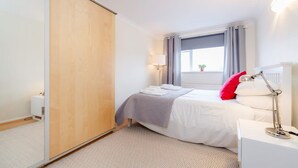 Ein Schlafzimmer mit Bett, Nachttischlampe, Fenster mit Vorhängen und Blick ins Freie.