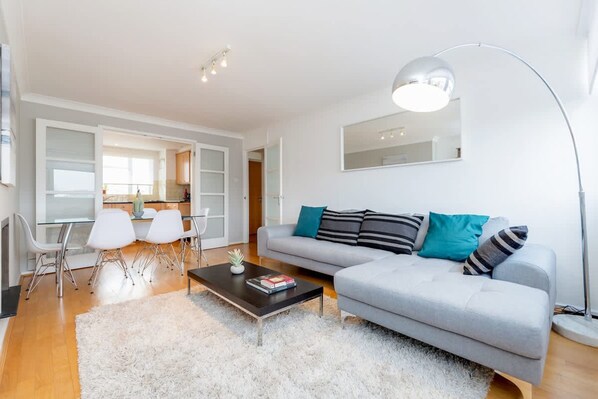 Un salon moderne avec un canapé gris, des fauteuils blancs, une table basse et un lampadaire.
