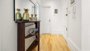 A hallway with a wooden console table, a mirror, and a white door at the end. - Beautiful 2bed Flat With Balcony in Earls Court (London)