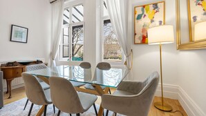 A dining area with a glass table and four chairs, a floor lamp, and a painting on the wall. - Beautiful 2bed Flat With Balcony in Earls Court (London)