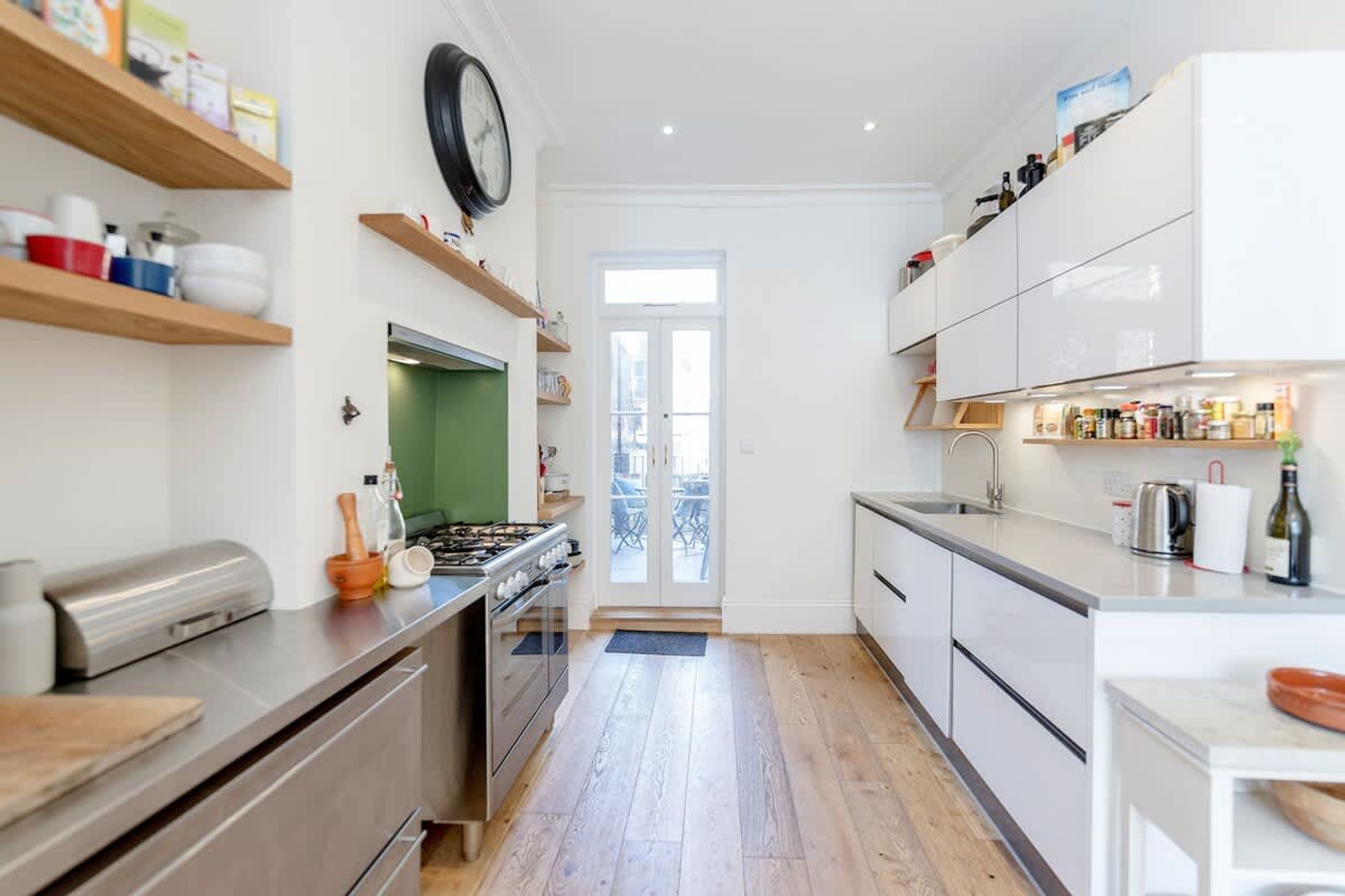A modern kitchen with wooden shelves, a gas stove, and white cabinetry.