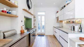 A modern kitchen with wooden shelves, a gas stove, and white cabinetry.