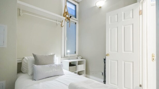 A bedroom with a bed, a bedside table, a window, and a door. - Beautiful Refurbished 2bed 2bath Next to Hyde Park (London)