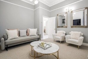 A living room with a grey sofa, two white armchairs, a marble coffee table, and two large mirrors on the wall. - Beautiful Refurbished 2bed 2bath Next to Hyde Park (London)