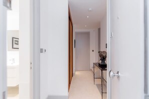 A narrow hallway with a wooden door on the left, a white door on the right, and a small table with a sculpture in the center. - Modern Stylish 2bed 2bath Close to Kings Road (London)