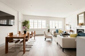 A spacious living room with a dining area, large windows, and a fireplace. - Modern Stylish 2bed 2bath Close to Kings Road (London)