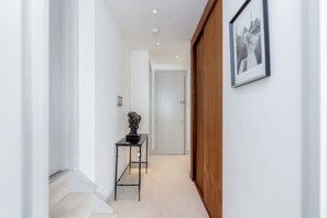 A hallway with a wooden door, a framed picture on the wall, and a small table with a sculpture. - Modern Stylish 2bed 2bath Close to Kings Road (London)