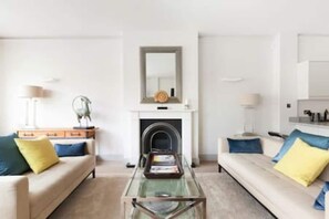 A modern living room with a glass coffee table, two sofas with cushions, a fireplace, and a mirror on the wall. - Modern Stylish 2bed 2bath Close to Kings Road (London)