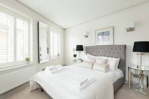 A modern hotel room with a large bed, bedside tables, and a window with blinds. - Modern Stylish 2bed 2bath Close to Kings Road (London)