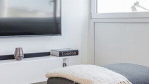 A modern living room with a flat-screen TV, a glass coffee table, a grey sofa, and a window with natural light. - Spacious 2bed in top Location Holland Park-n Hill (London)