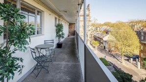 A balcony with a table and chairs, potted plants, and a view of a residential street. - Spacious 2bed in top Location Holland Park-n Hill (London)
