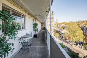 A balcony with a table and chairs, potted plants, and a view of a residential street. - Spacious 2bed in top Location Holland Park-n Hill (London)