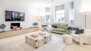 Una sala de estar moderna con un televisor de pantalla plana, un sofá verde, un sillón blanco y una mesa de centro con libros.