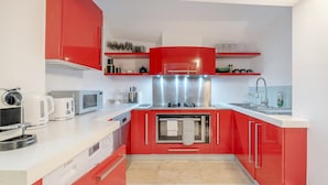 Una cocina compacta con armarios rojos, un microondas, un tostador y un lavamanos.