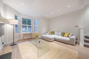 A modern living room with a sofa, a coffee table, a lamp, and a TV. - Stylish 3-floor 3bed Home With Garden Near River (London)