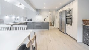 A modern kitchen with a central island, built-in appliances, and a dining area with a white table and chairs. - Stylish 3-floor 3bed Home With Garden Near River (London)