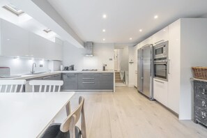Eine moderne Küche mit einer zentralen Kochinsel, integrierten Geräten und einem Essbereich mit weißem Tisch und Stühlen.