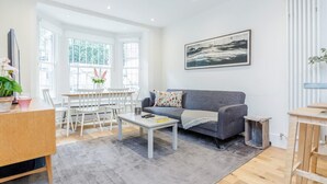 Ein modernes Wohnzimmer mit grauem Sofa, weißem Couchtisch und einem Essbereich mit weißen Stühlen und einem Tisch.
