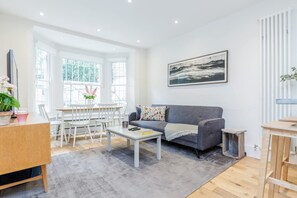 Ein modernes Wohnzimmer mit grauem Sofa, weißem Couchtisch und einem Essbereich mit weißen Stühlen und einem Tisch.