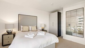 A modern bedroom with a large bed, two bedside tables with lamps, a large mirror, and a view of the outside through a window. - Luxury and Quiet Oasis in London (London)
