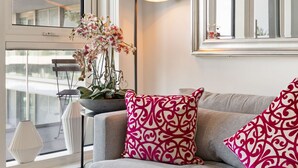 A modern living room with a grey sofa, patterned pillows, a glass coffee table, a floor lamp, and a large window offering a view of the building's exterior. - Luxury and Quiet Oasis in London (London)
