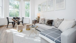 A bright living room with a sofa, a coffee table, and a dining area with chairs and a table. - Charming Spacious 1bed Near Portobello Rd N Hill (London)