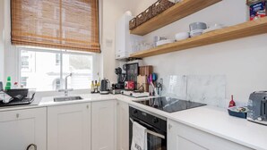 A modern kitchen with white cabinets, a black stove, and a window with blinds. - Charming Spacious 1bed Near Portobello Rd N Hill (London)