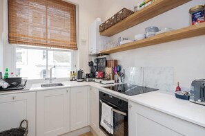 Moderni keittiö, jossa on valkoiset kaapit, musta liesi ja ikkuna, jossa on sälekaihtimet.